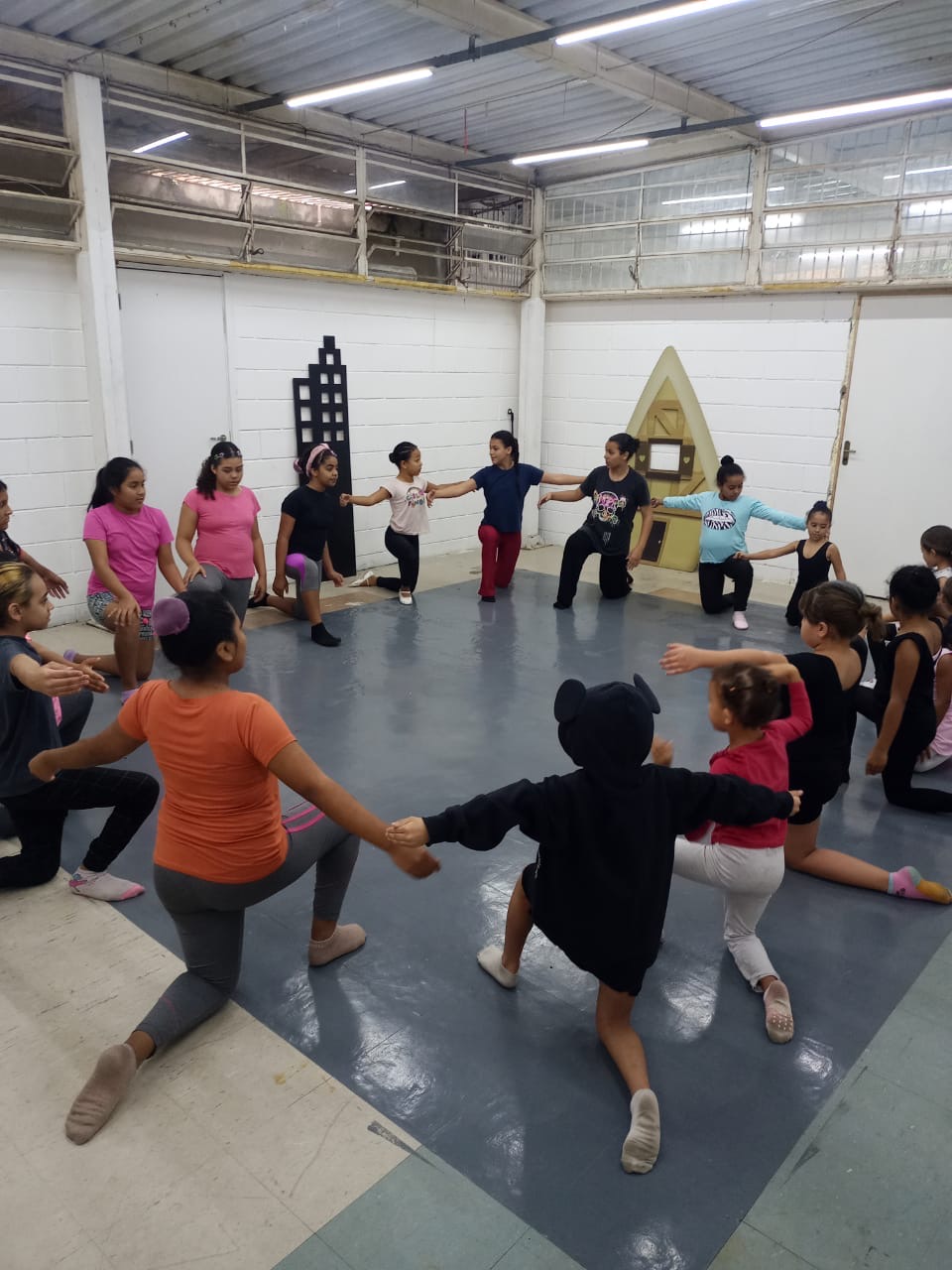 Participantes em círculo fazendo exercício de alongamento com braços estendidos em sala de aula de balé