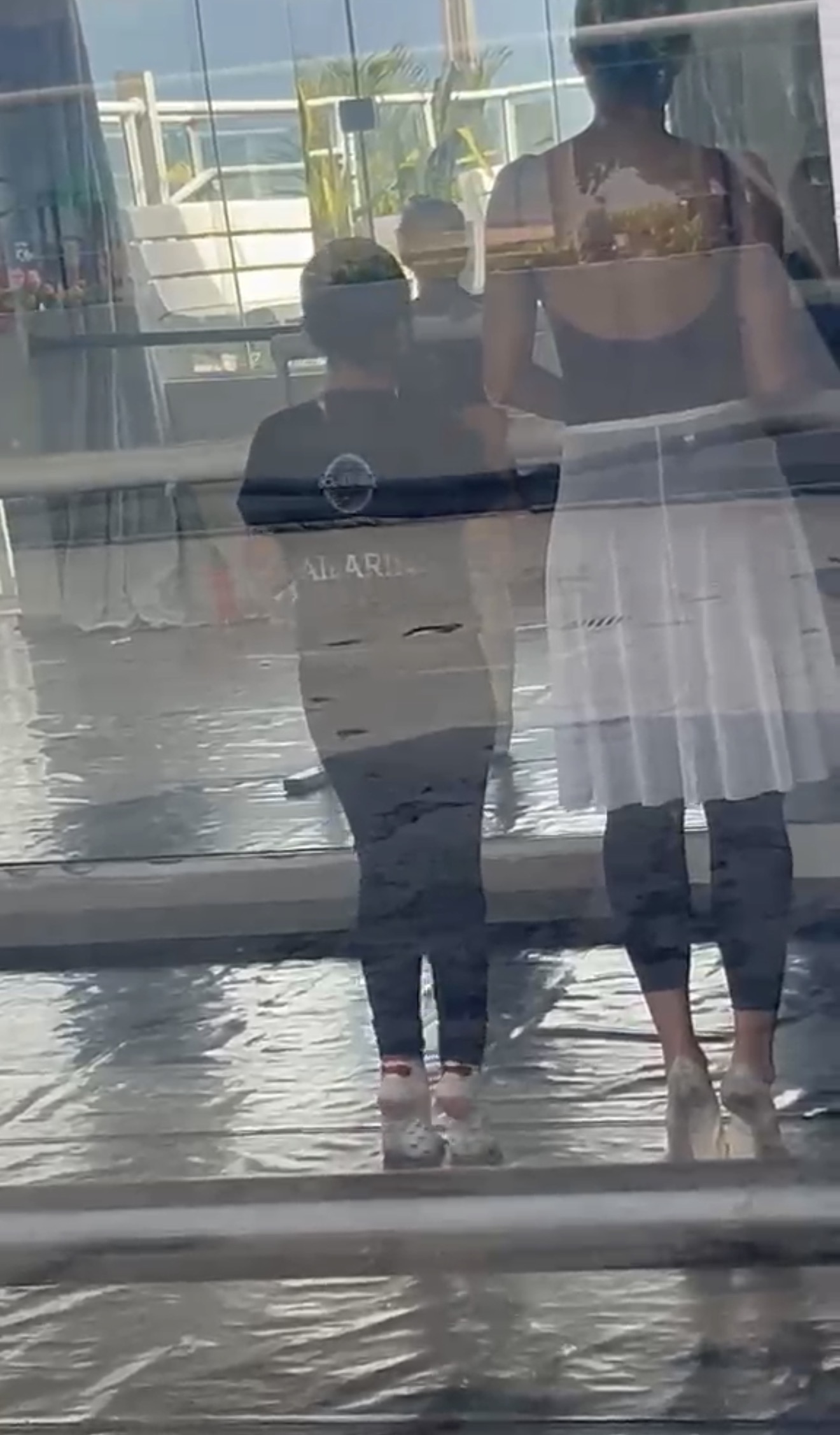 Reflexo no espelho de uma criança e de uma bailarina de saia branca lado a lado durante aula de balé