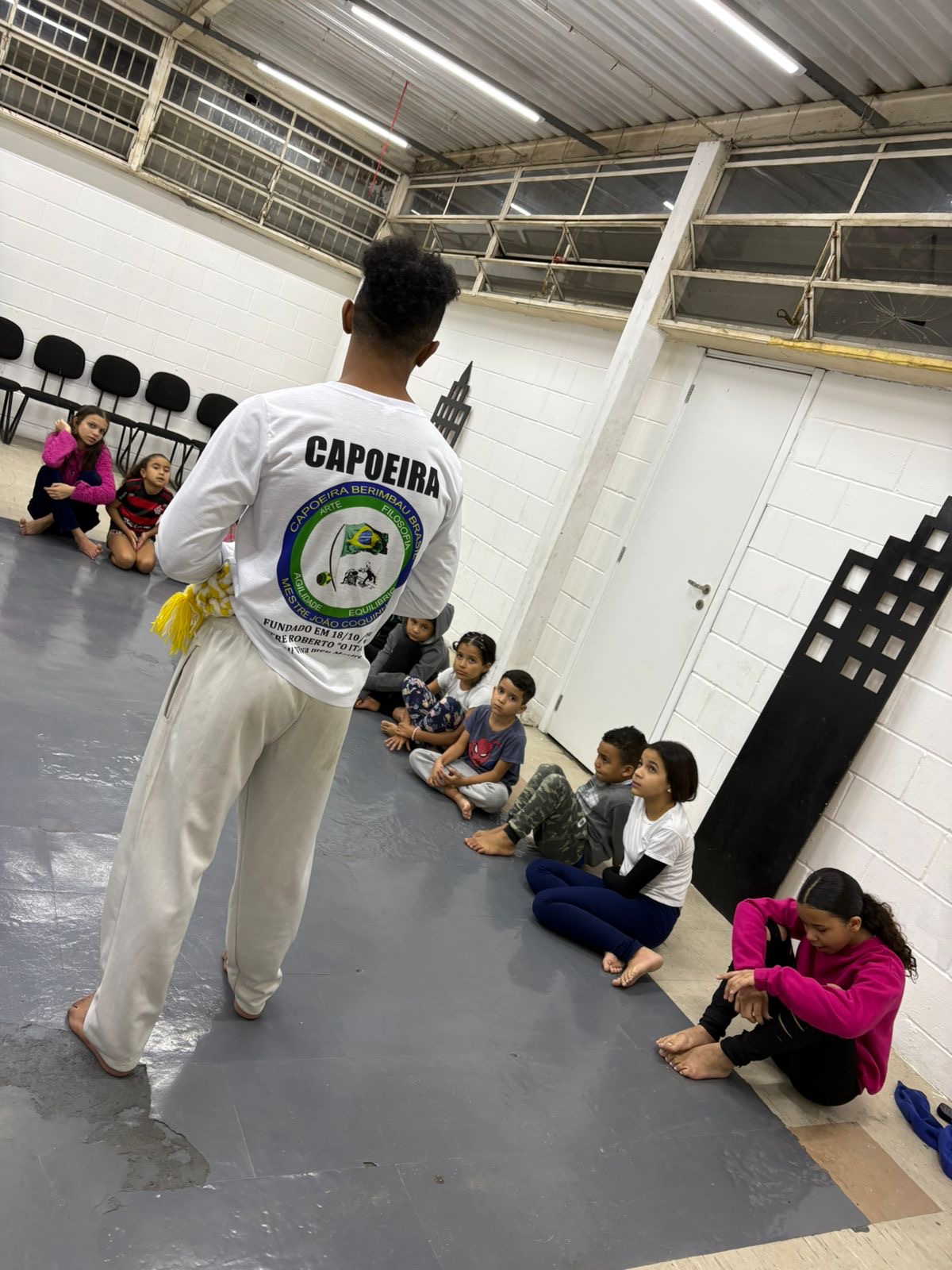 Instrutor conversando com participantes sentados durante a aula de Capoeira