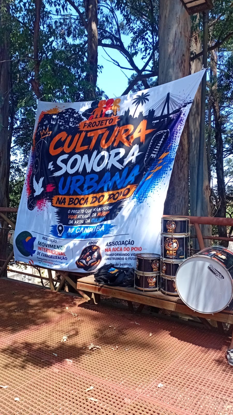 Banner do Projeto Cultura Sonora Urbana Na Boca do Povo, com realização do MIDE, ao lado de instrumentos de percussão
